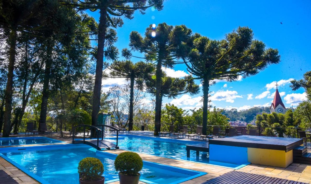 piscinas no alto de morro com árvores tipo araucária no ao fundo