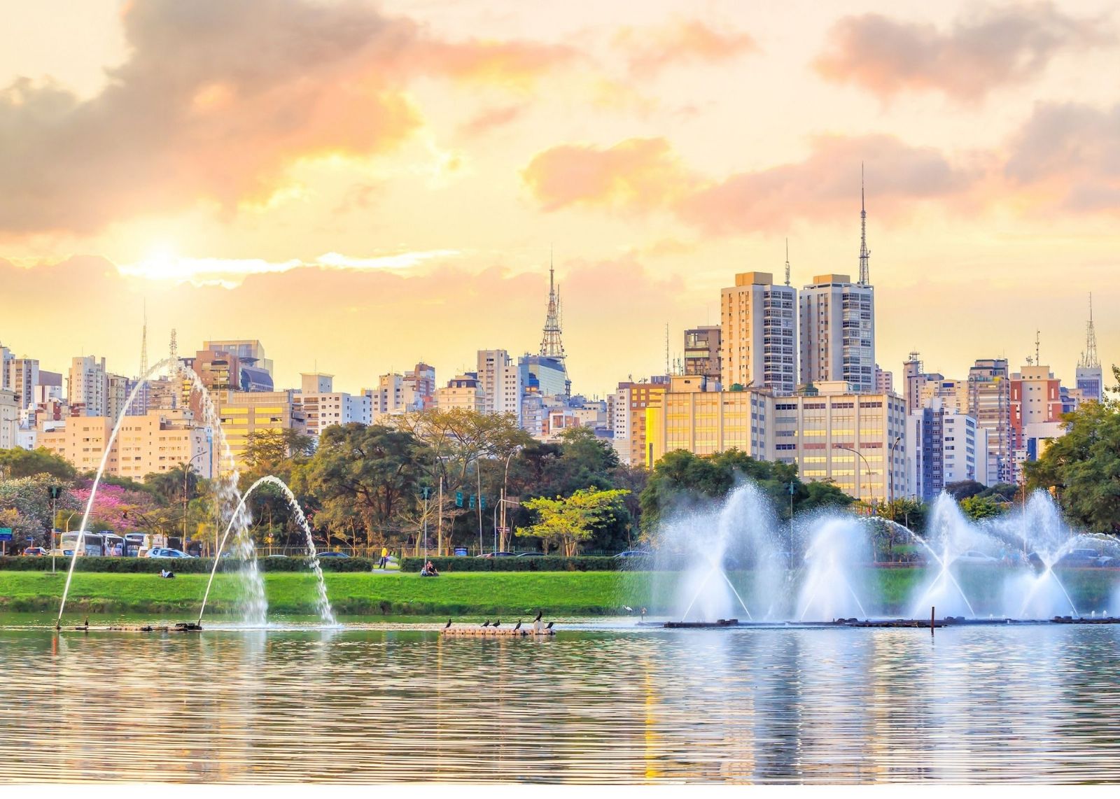 lago com fontes e parque com skyline de por do sol no fundo