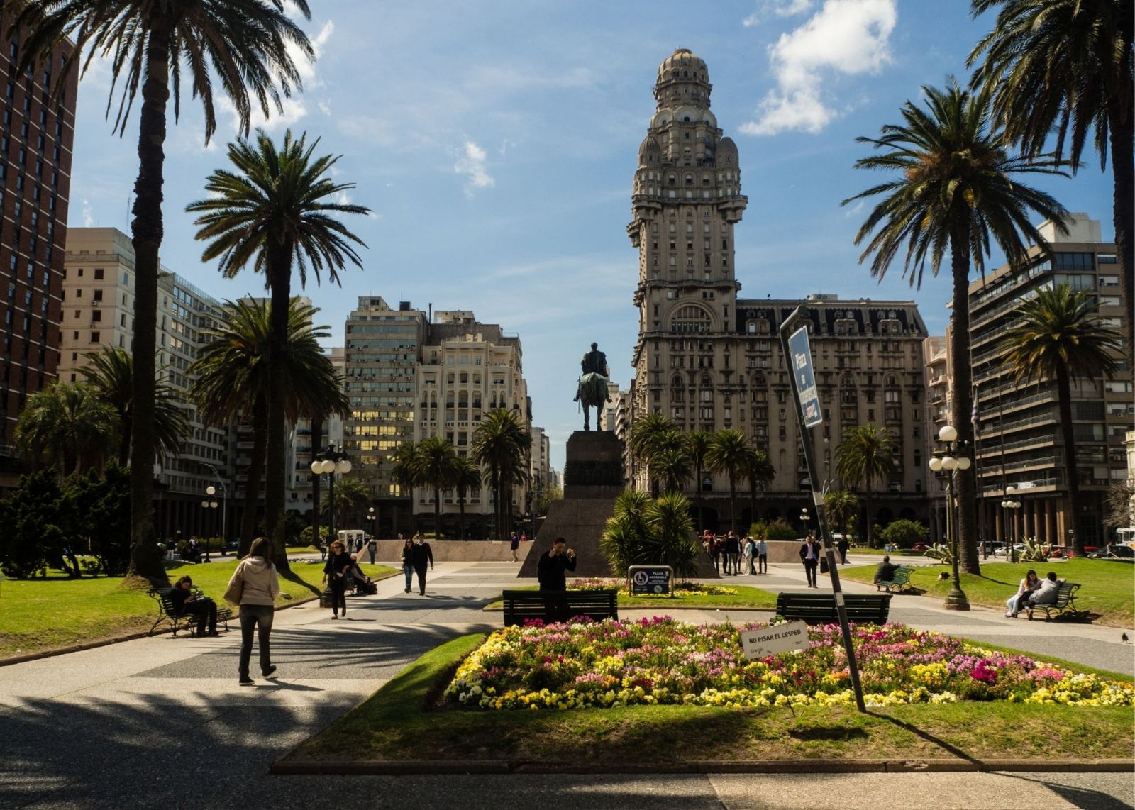 praça com arvores e estatua de cavalo e cavaleiro com prédios no fundo