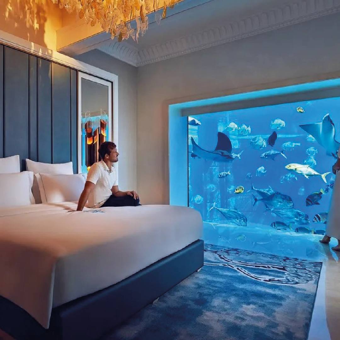 homem sentado em uma cama observando grande aquário
